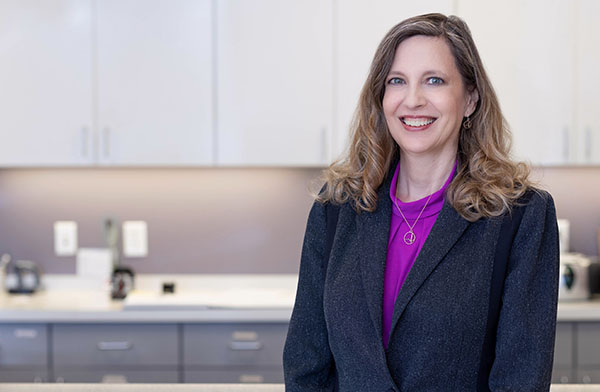 Dr. Susan Mosier is a caucasian woman with a dark jacket and pink shirt standing in front of a medical office check-in desk.