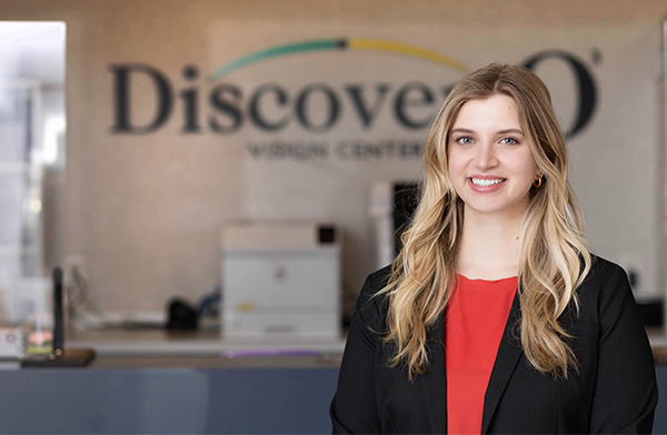 Dr. Rachel Newland, caucasian woman with blonde hair stands in front of a check-in desk wearing a black jacket and red blouse.