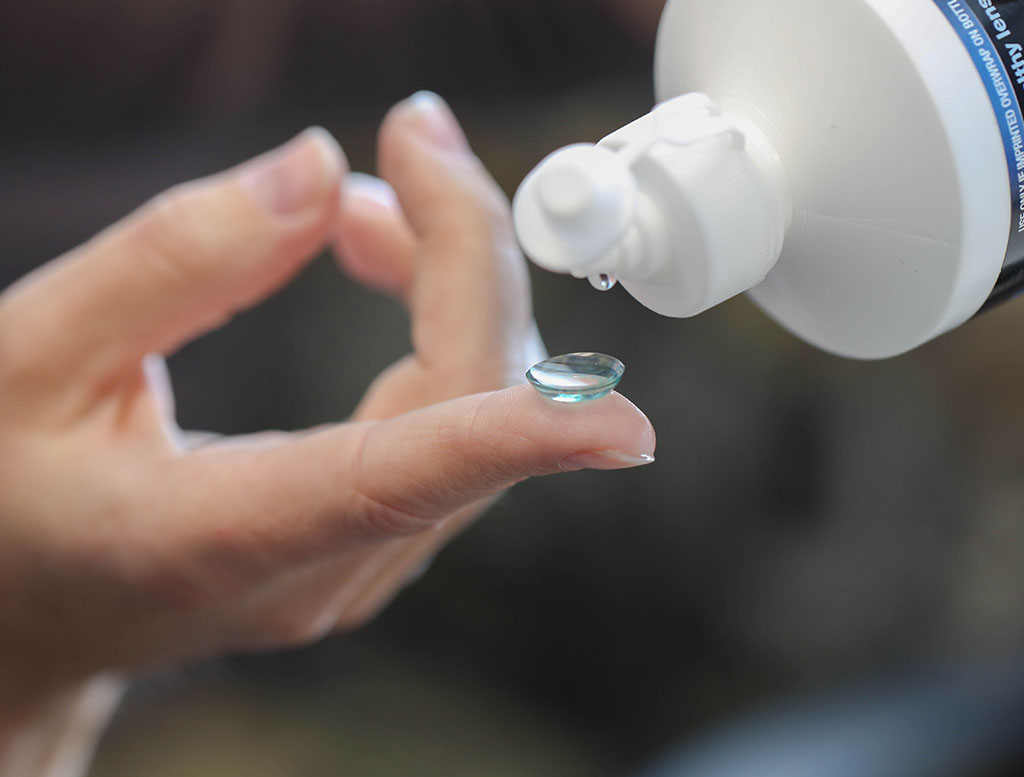 Contact Lens Tips from Discover Vision: Hand is shown with contact lens on pointer finger and contact lens solution in a white bottle dropping onto the contact.