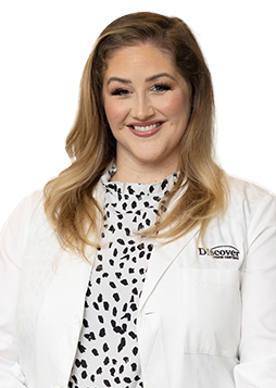 Dr. Jessica Fowler is a caucasian woman with blondish brown hair standing against a white background. She is wearing a white doctor coat and a white blouse with black dots.