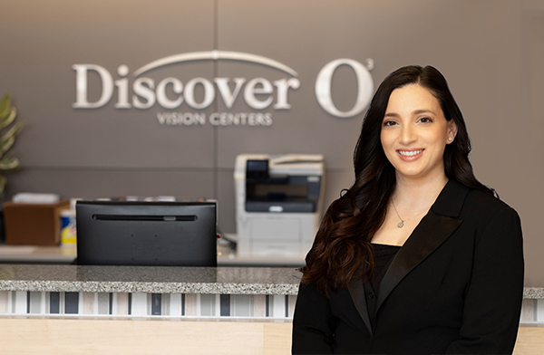 Dr. Suzanne Adkins is a caucasian woman wearing a black suit standing in front of a brownish purple wall with a Discover Vision logo behind her.