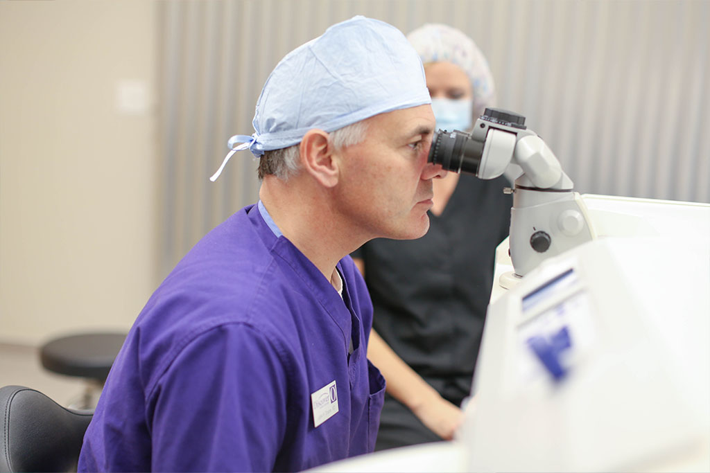 Doctor wearing purple scrubs performing LASIK surgery, looking through the Zeiss laser microsocope.