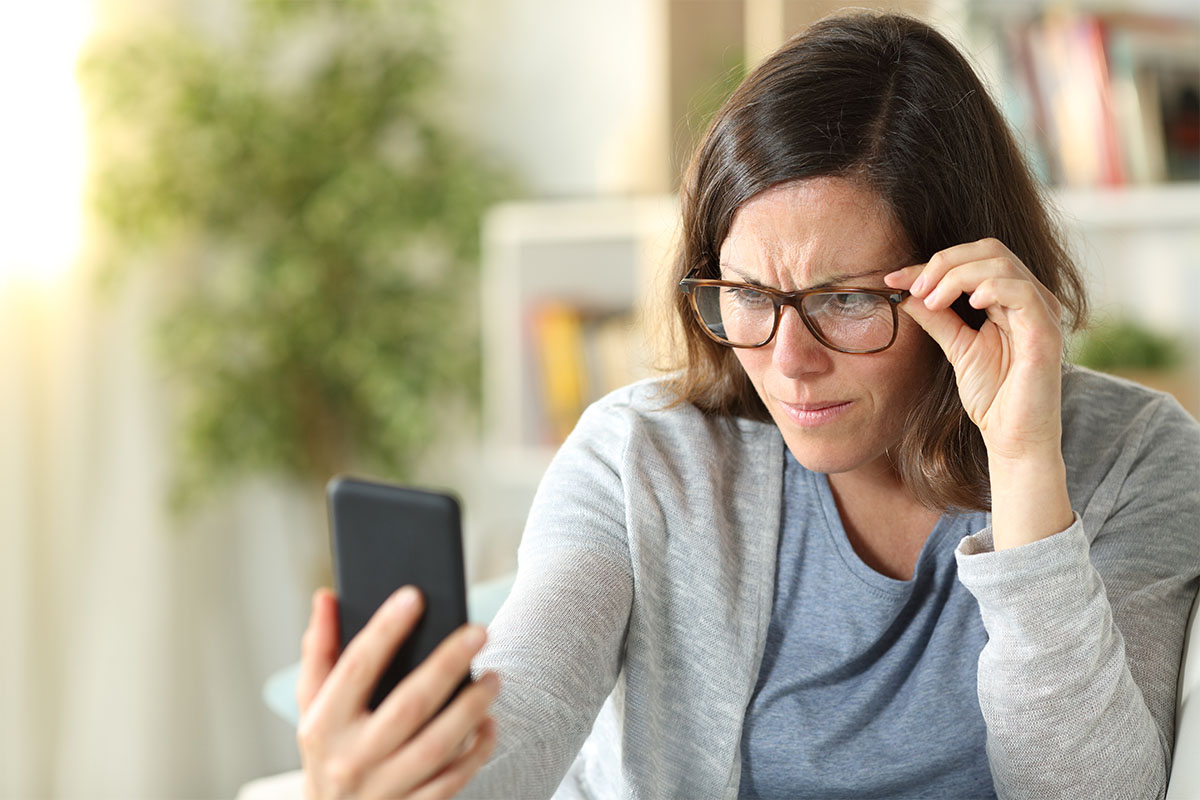 LASIK Eye Surgery for Presbyopia | Woman sin a grey sweater and blue shirt strains to read her cell phone.