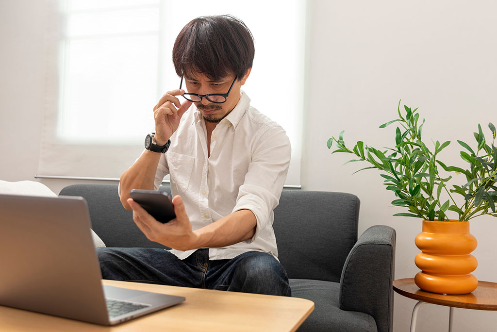 Alternative Types of Presbyopia Treatments | Person wearing a white button up shirt with black reading glasses struggles to read their phone, holding it at arms length.