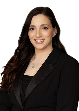 A caucasian woman with dark hair in a black suit stands against a white background