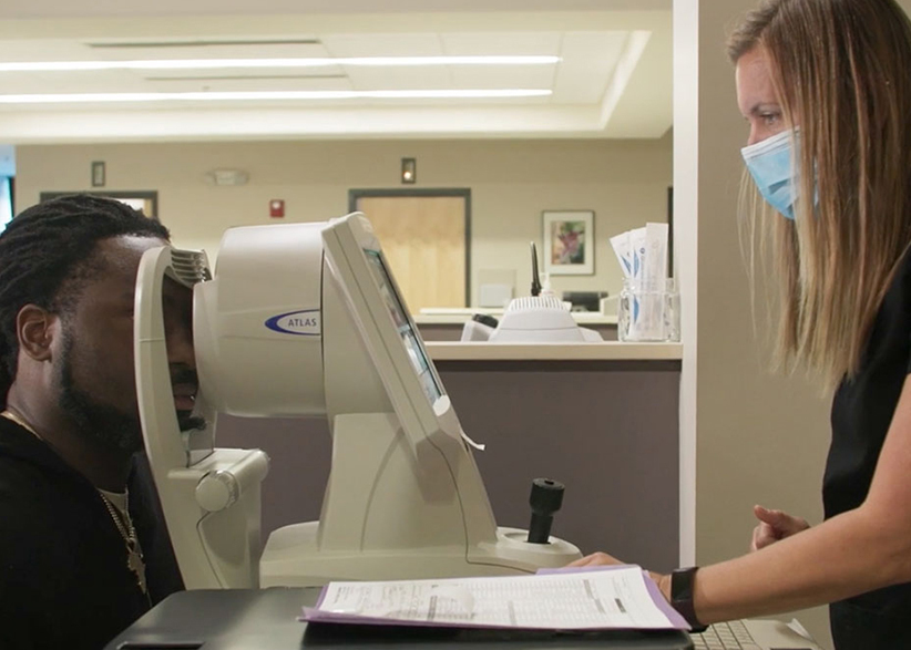 A caucasian woman with blond hair wearing a black shirt provides a LASIK test to football player Derrick Nnadi